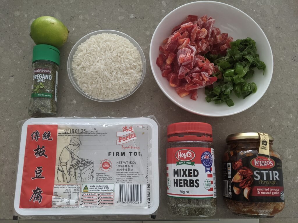 Cette image montre les ingrédients essentiels pour préparer une garniture de fajitas vegan rapide, savoureuse et pleine de protéines. On y retrouve du tofu ferme, des poivrons rouges frais, des cébettes, de la sauce tomate, des herbes de Provence, de l'origan, ainsi que des épices citronnées pour relever le tout. Idéale pour une recette de fajitas vegan simple, économique et parfaite pour un repas convivial et healthy. Parfaite pour ceux qui souhaitent préparer des repas équilibrés avec des ingrédients facilement disponibles à la maison.
